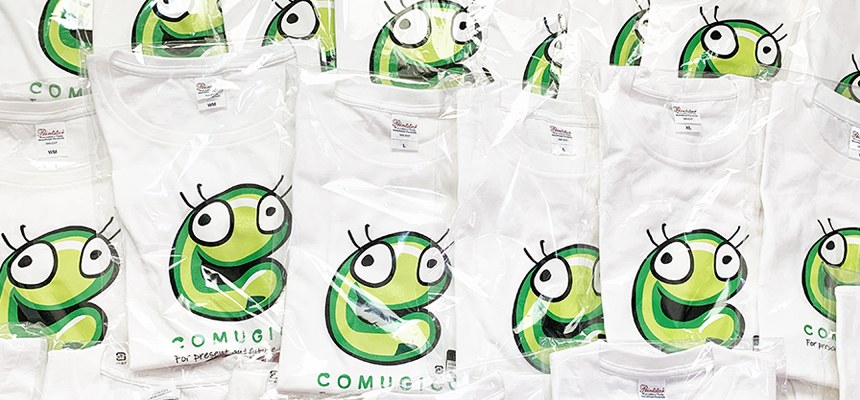 COMUGICOのキャラクターのロゴを胸の真ん中に大きく入れた白いTシャツがたくさん並んでいる