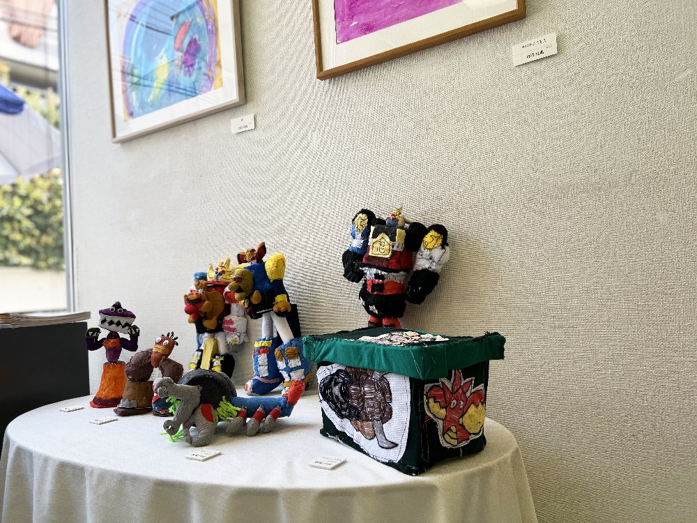 丸いテーブルの上に並ぶ、ロボットなどカラフルな立体作品