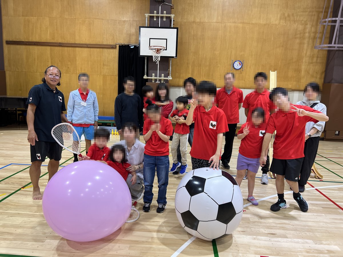 体育館で、大きなピンクのボールとサッカーボールをかこんで並ぶ、参加した子どもたちとBLACKSOXのスタッフ・サポーターのみなさん