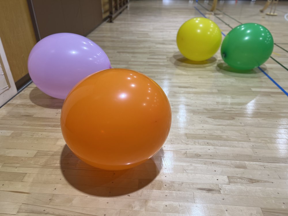 体育館の床に転がる、むらさき・オレンジ・黄色・緑の大きな風船