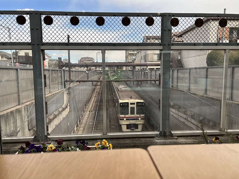 テーブルの先のフェンスごしに見下ろす、地下へ続く線路と電車