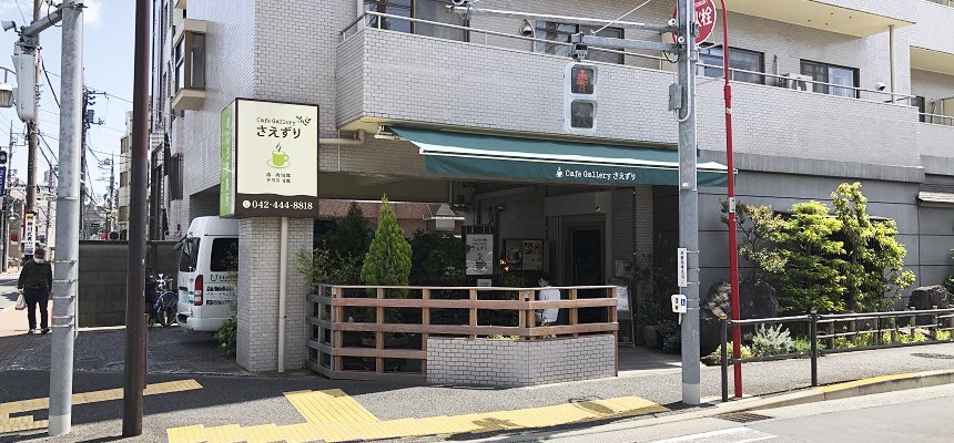 交差点の角のマンション1階にある、緑のオーニングテントとテラス席のお店の外観