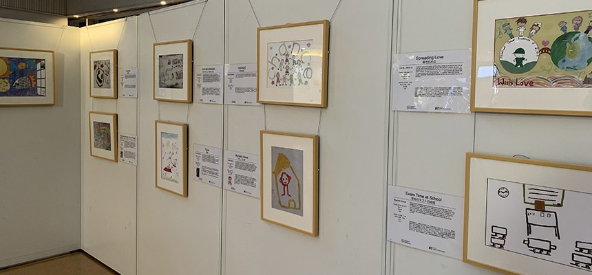 白い壁に、額に入った子どもたちの絵と説明文が並ぶ展示のようす
