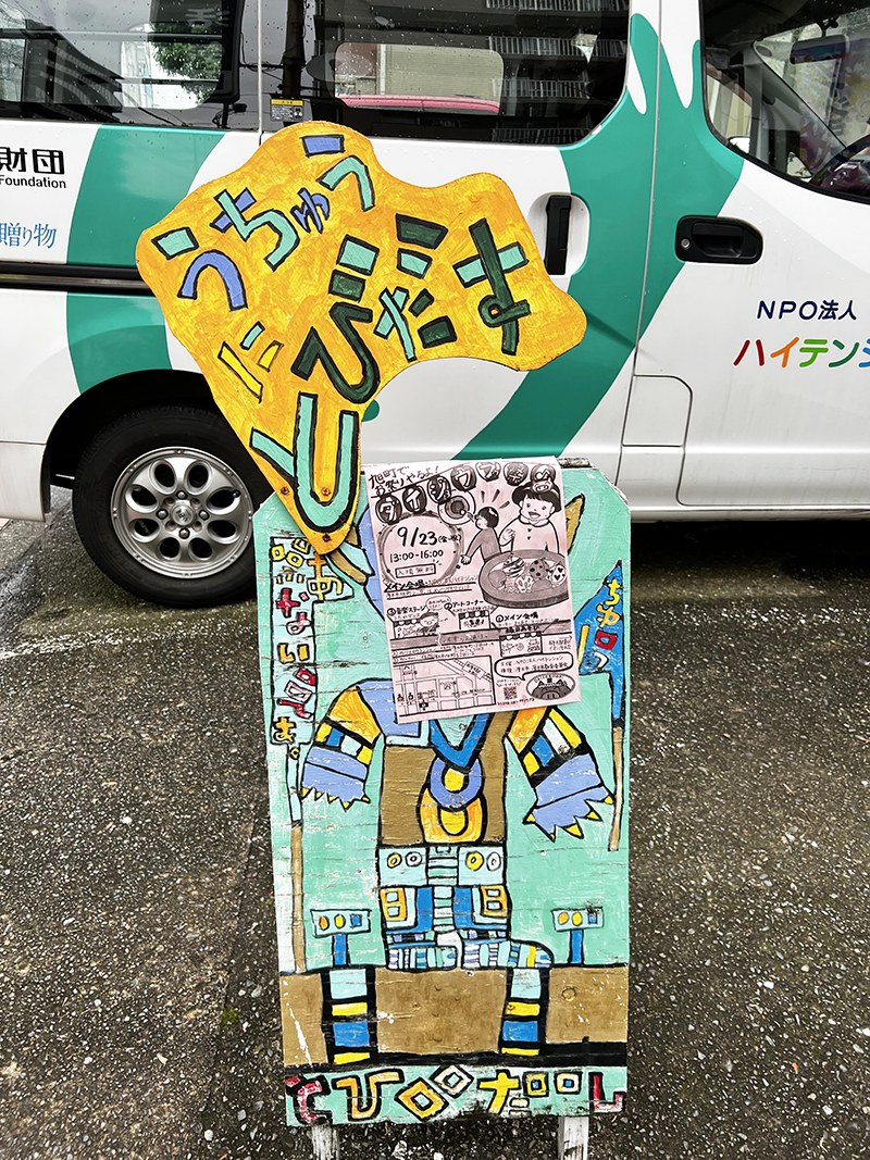 カラフルな手描きの看板に、お祭りのチラシが貼られている