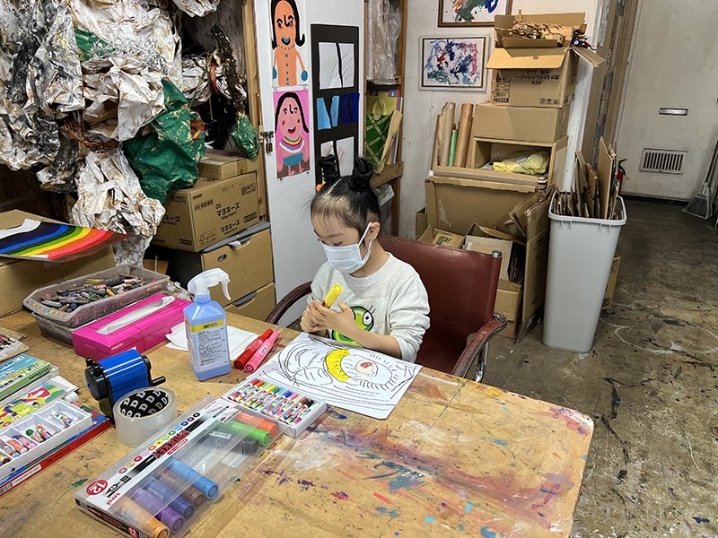 絵の具が飛び散った机で、マーカーを使ってお絵描きをする娘