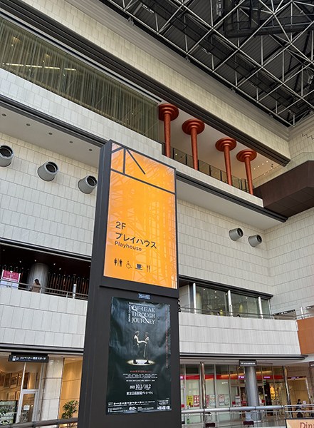 「2F プレイハウス」の案内表示と公演ポスターが立つ劇場のアトリウム