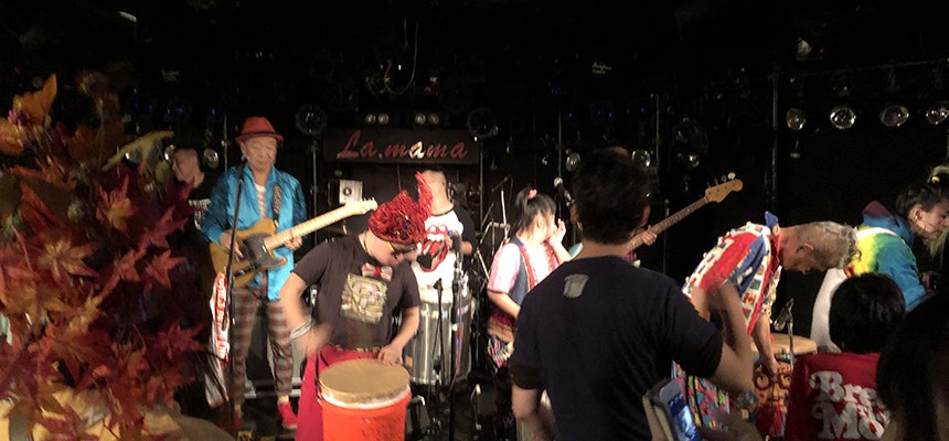 紅葉の飾りのステージで、太鼓やギターを演奏するサルサガムテープ