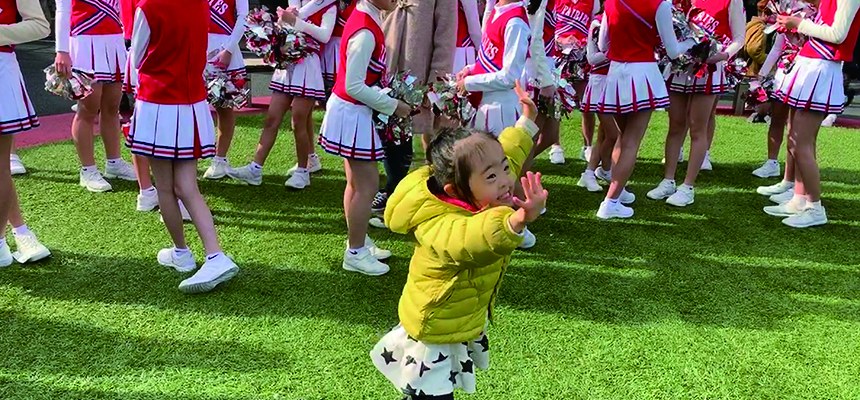 チアダンスのグループのそばで、手を合わせて体を動かす娘