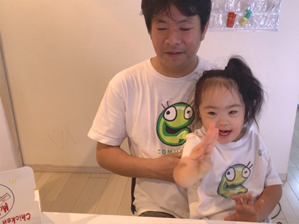 パソコンの前で父親のひざに座り、画面に向かって手を振って笑う娘