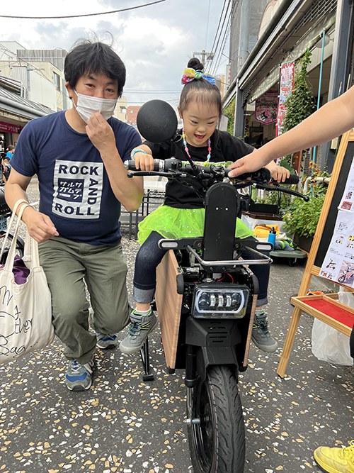 コンパクトな電動バイクにまたがる娘と、横で支える男性
