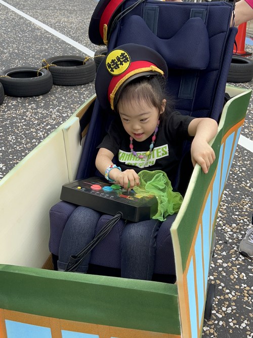 電車の形に改造された電動車いすに、運転手の帽子をかぶって乗る娘