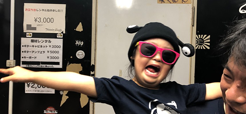楽屋で、触角の付いた帽子とピンクのサングラスをつけて両手を広げる子ども
