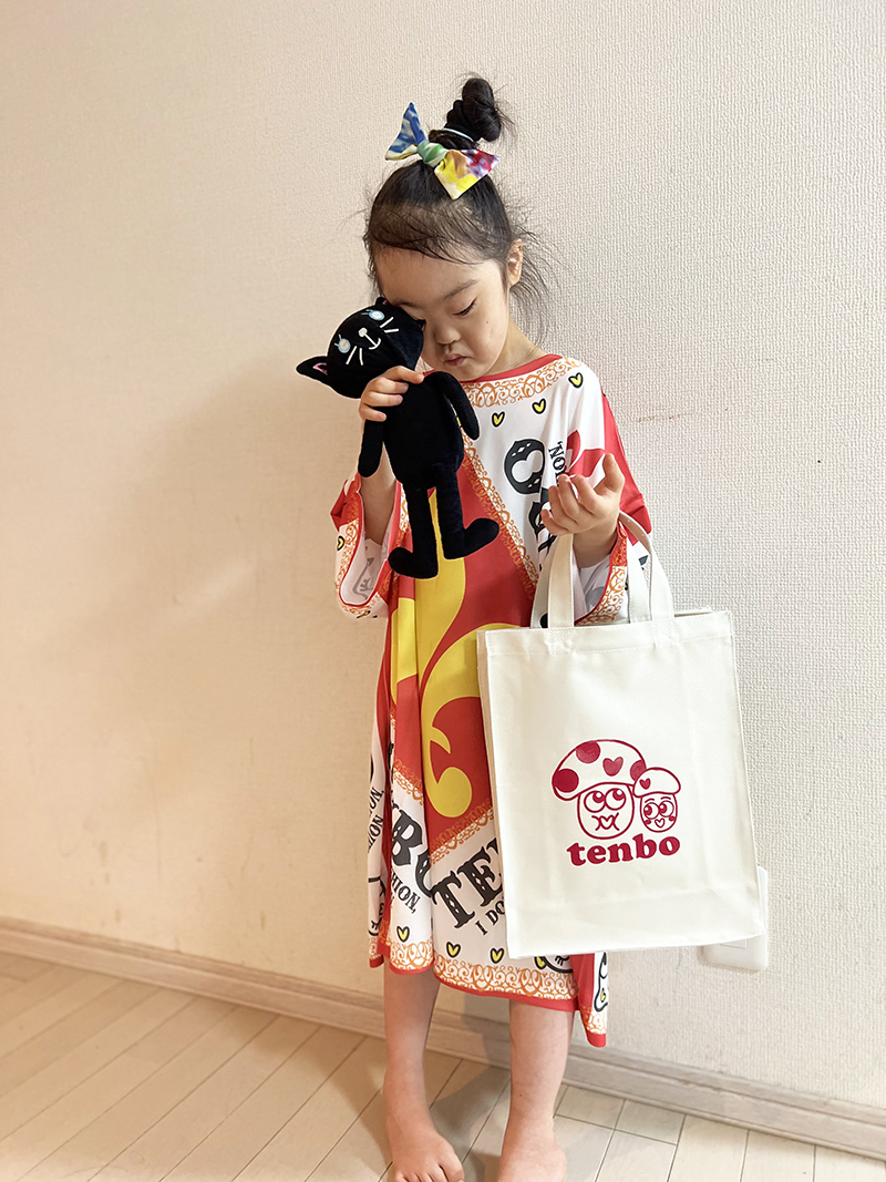 大きなTシャツをワンピースのように着て、tenbo のトートバッグを持ってポーズをとる子ども