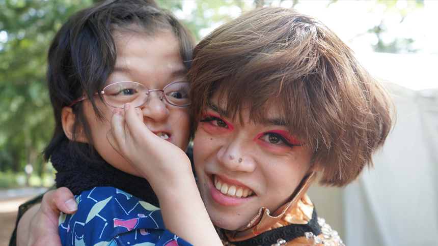 和柄の衣装を着た子どもと、メイクをしたスタッフが頬を寄せて笑っている
