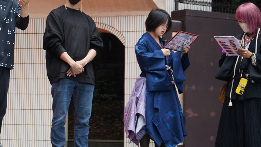 会場の入り口で、青い衣装を着たモデルたちがパンフレットを手に立っている
