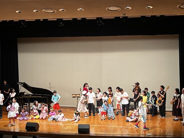 ホールのステージに、出演した子どもたちと先生、サポートのミュージシャンが全員そろっているエンディングのようす