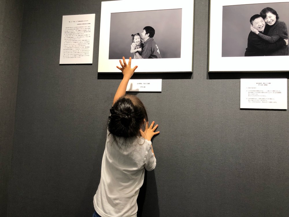 壁に飾られた自分の写真に手を伸ばす娘の後ろ姿