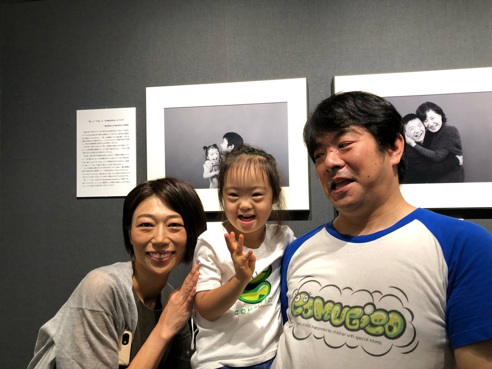 展示写真の前で、葛谷さんと娘と父の3人が笑う記念写真