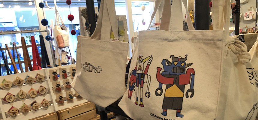 ロボットの絵がプリントされたトートバッグと、木のブローチが並ぶ棚