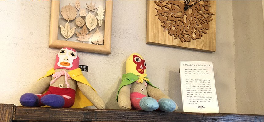 棚に座る2体のプロレスラーのぬいぐるみと、木の作品の額