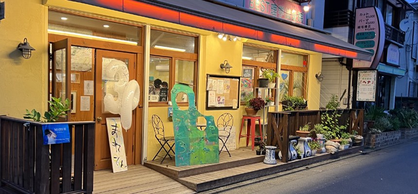 黄色い外壁のカフェ「POSTO」の外観。入口に風船や看板が並ぶ