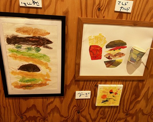 木の壁に飾られた、ハンバーガーを描いた絵などの作品