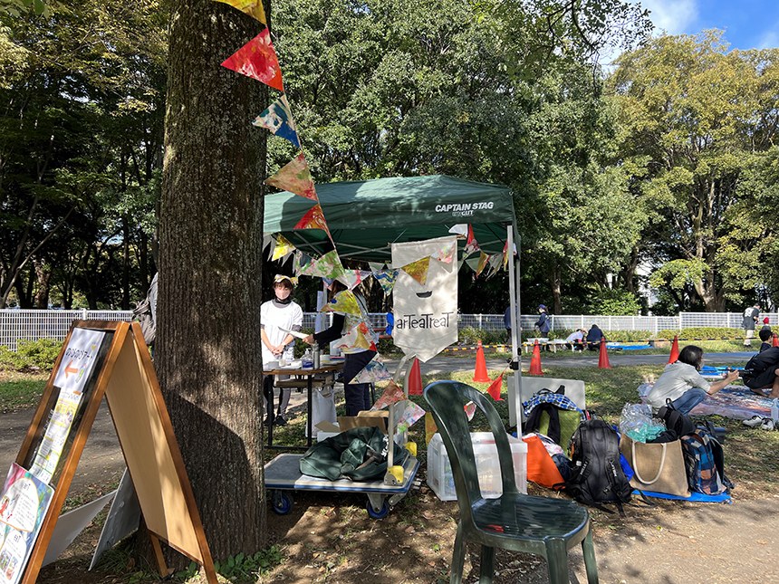 木に三角の旗が飾られ、テントと看板が立つアートイベントの会場