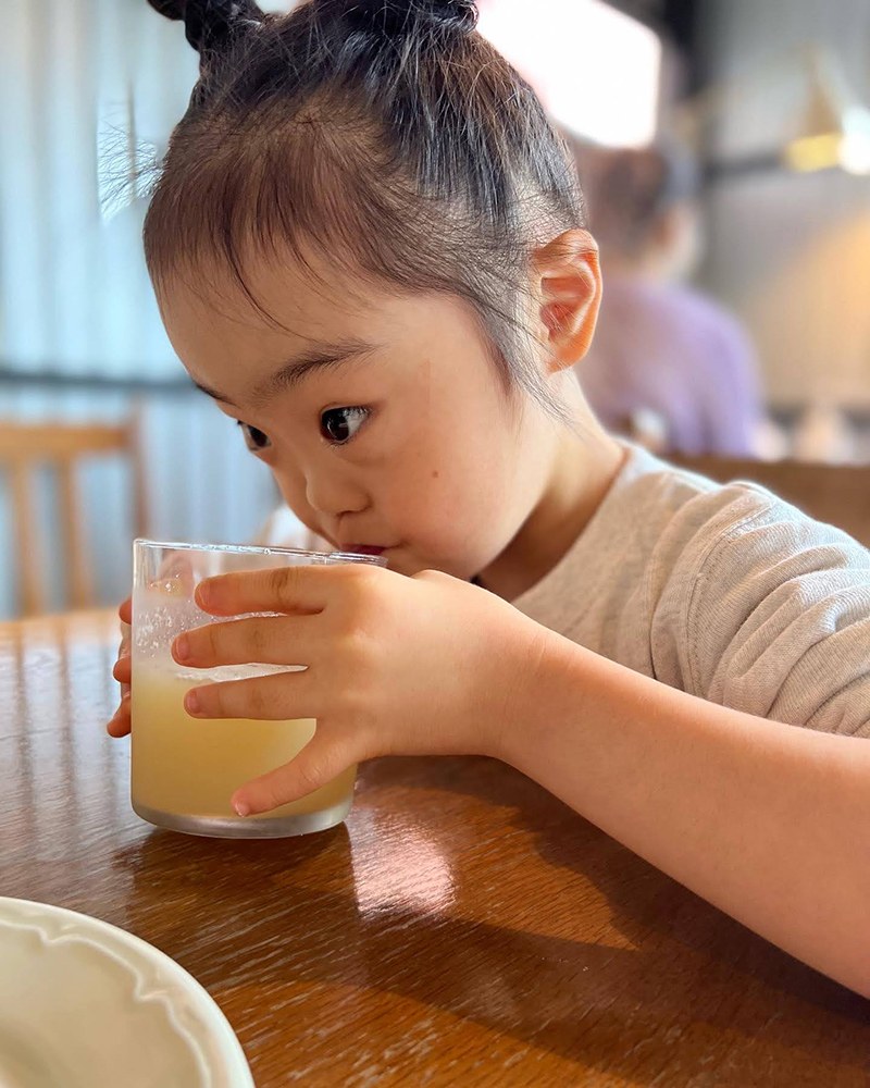 コップに入ったリンゴジュースを両手で持って飲む娘