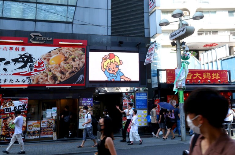 飲食店が並ぶ通りのビルのビジョンに映る、笑顔のキャラクターのイラスト