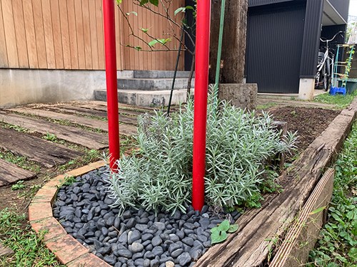 玄関前の植え込み。黒い玉石と赤い2本の柱のあいだにハーブが植えられている