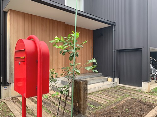 木の外壁の家の前に立つ赤いポスト