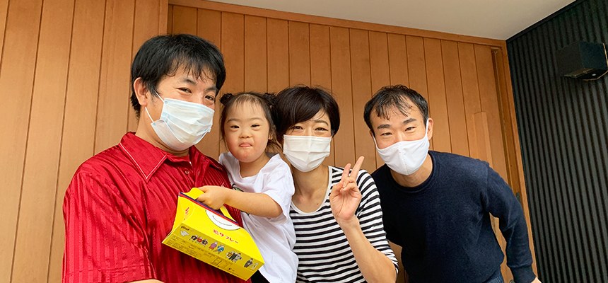 スタジオの入口の前で、マスク姿の大人3人と娘が並ぶ記念写真