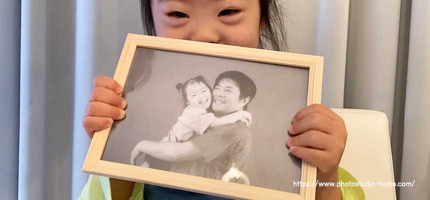 白木のフォトフレームに入った父と娘のモノクロ写真を持つ子ども