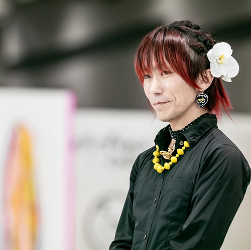 髪に白い花を飾り、黒い服を着た tenbo のデザイナー