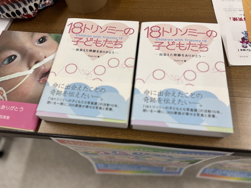 机に並んだ写真集『18トリソミーの子どもたち ―出会えた奇跡をありがとう―』(Team18 編)2冊。帯には「命に出会えたことの奇跡を伝えたい」とある