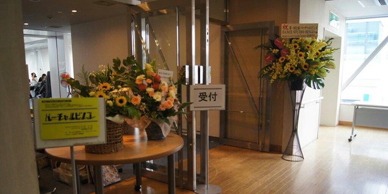 「バーチャルビンゴ」の札とひまわりの花が飾られた会場の受付