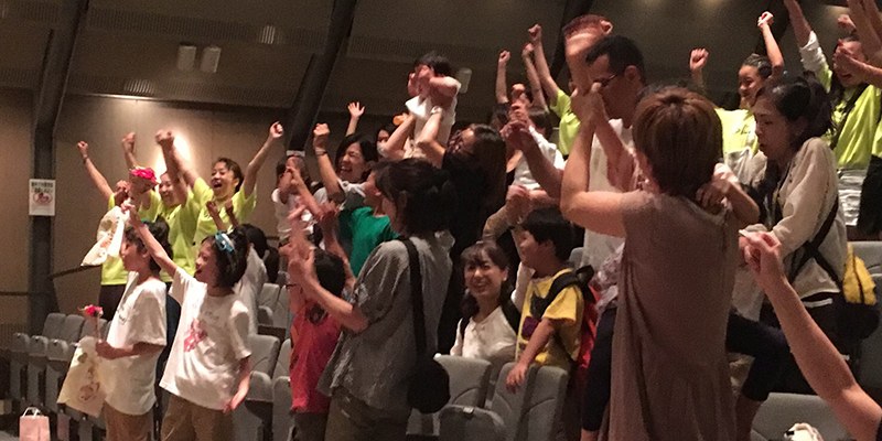 黄色いTシャツを着て、客席で拳を上げて盛り上がる出演者たち