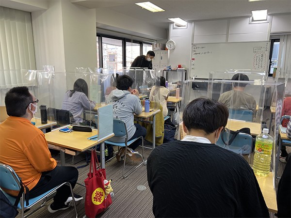 透明なパネルで仕切られた机に向かう生徒たちの教室