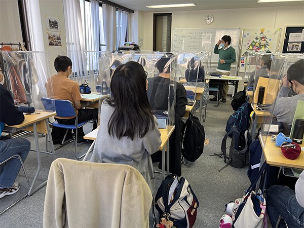 前に立つ先生の話を、パネルで仕切られた席で聞く生徒たち